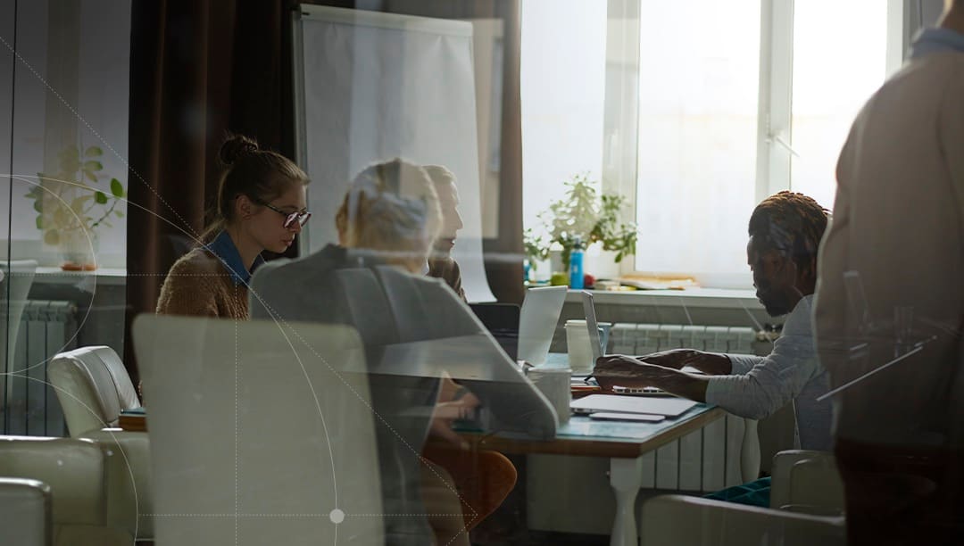 A team working around a meeting table, seen through a glass partition.